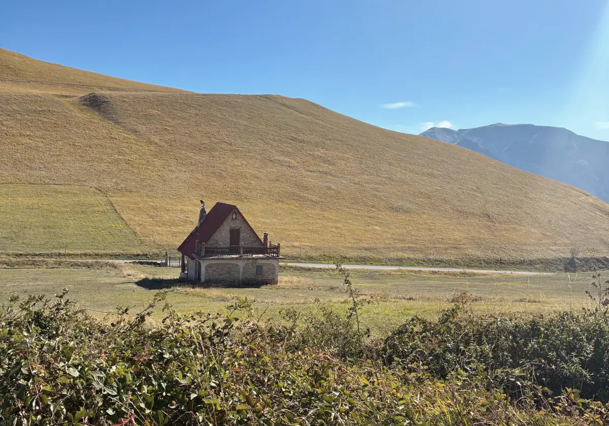 Una piccola casa di pietra in mezzo al prato, ai piedi di un pendio